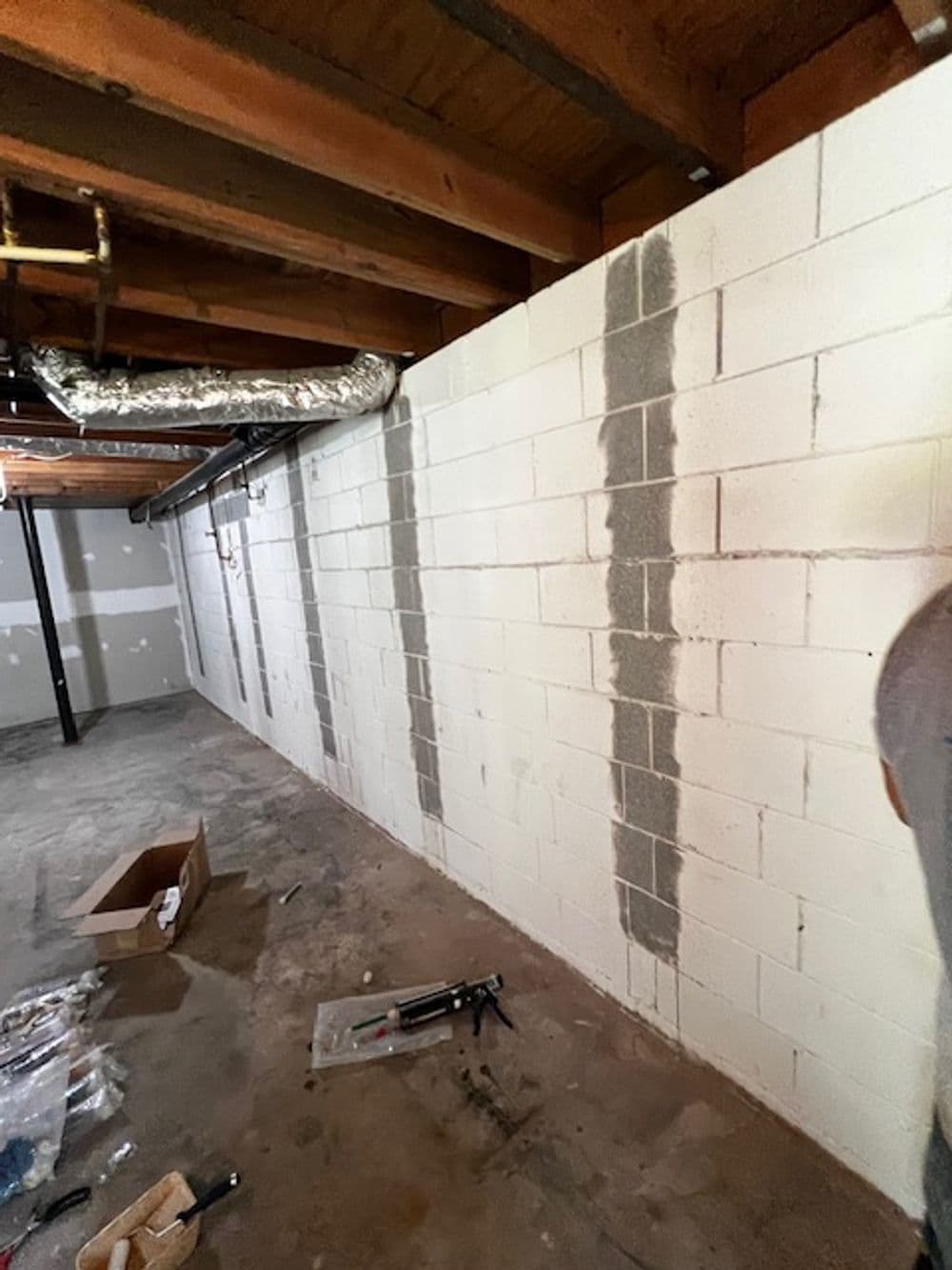 Basement wall with freshly applied gray waterproofing sealant and exposed wooden beams.