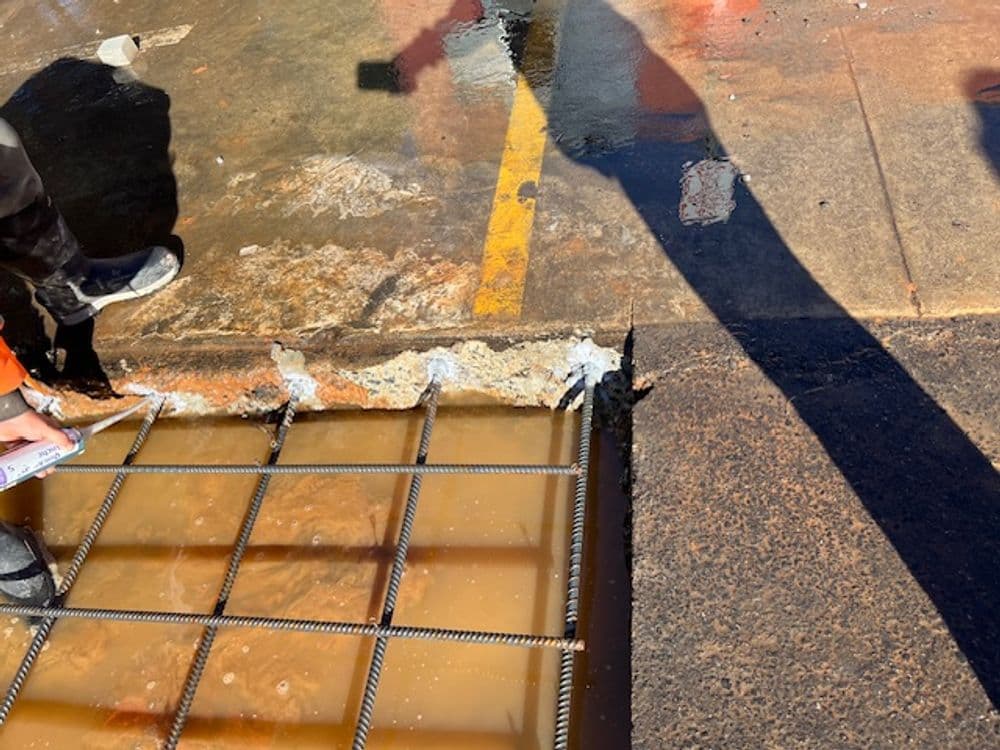 Construction worker inspecting rebar framework in flooded concrete area at a construction site.