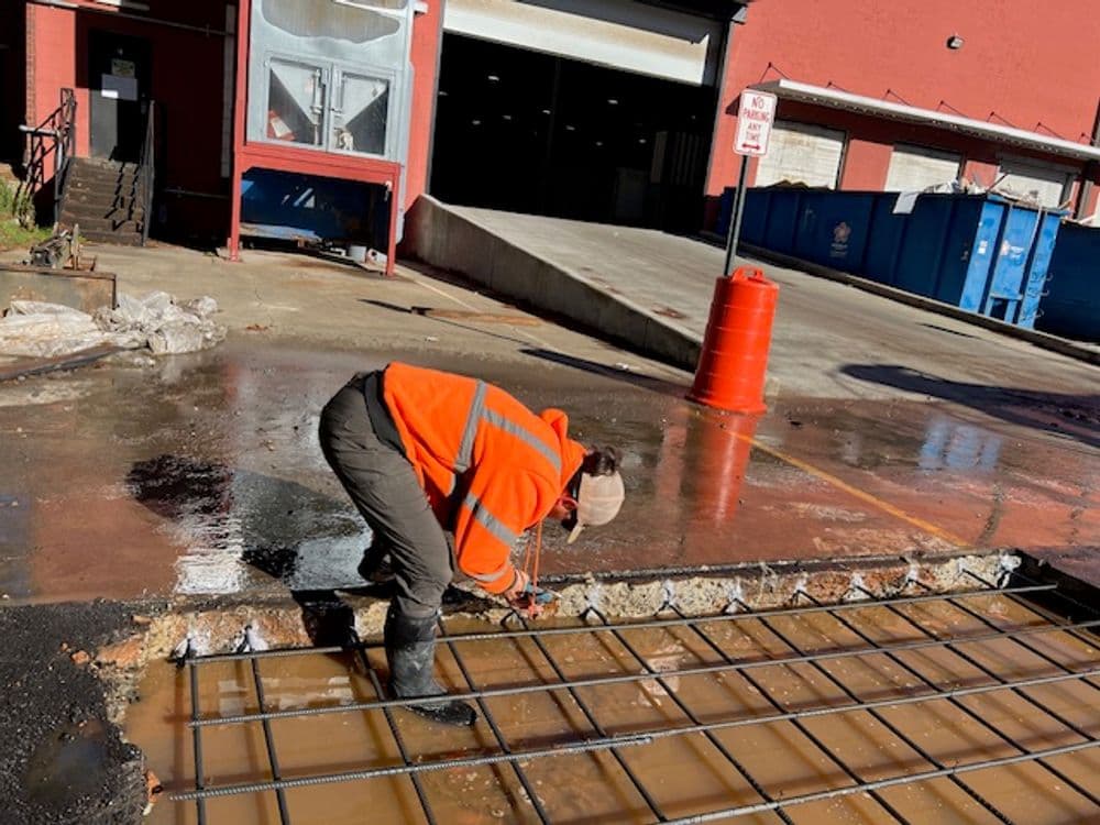 Worker laying concrete reinforcement in a construction site with water pooling on the ground.