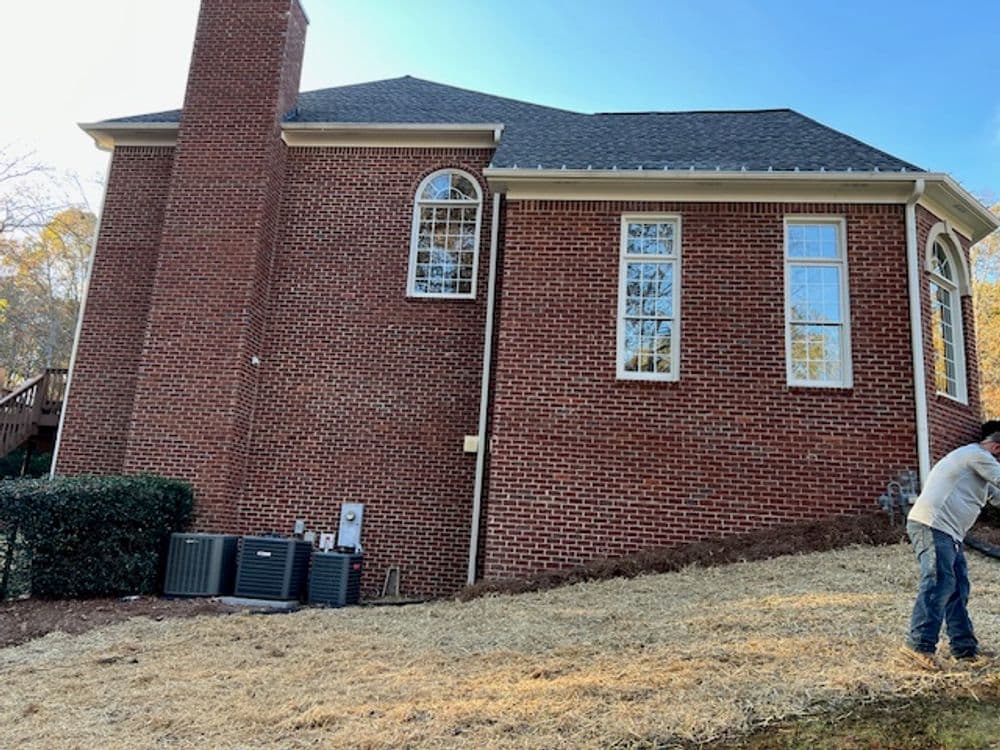 Brick house exterior with large windows and HVAC units in the yard, planting area prepared.