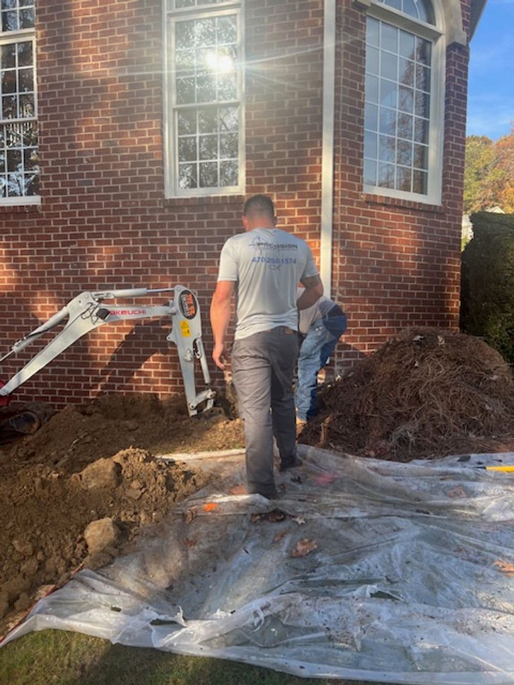 Construction workers digging near a brick building for landscaping or foundation repair.