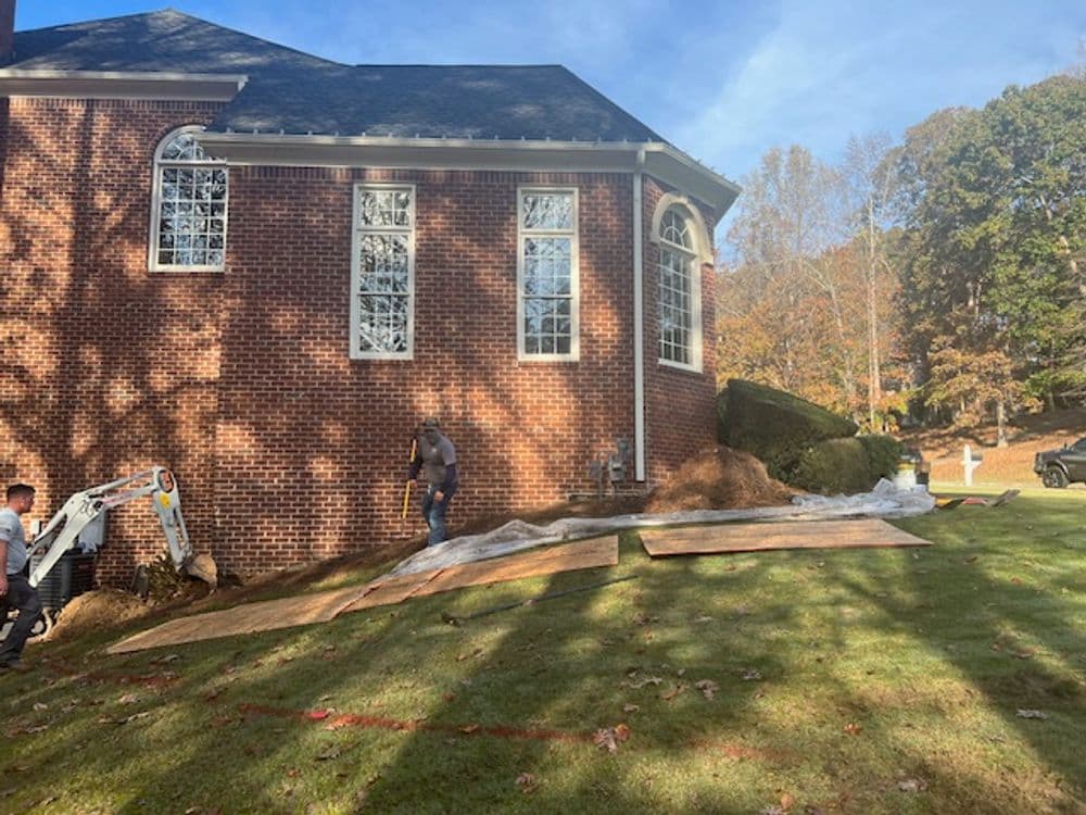 Construction workers installing landscaping near a brick house on a sunny day.
