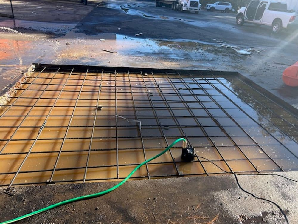 Construction site with wet concrete foundation, rebar grid, and water pooling.