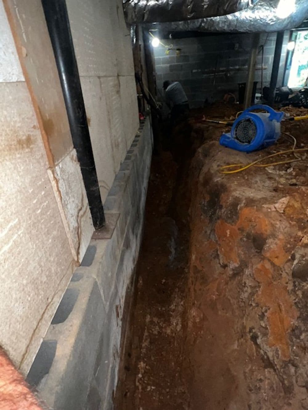 Excavation site showing a deep trench, construction tools, and equipment in a basement setting.