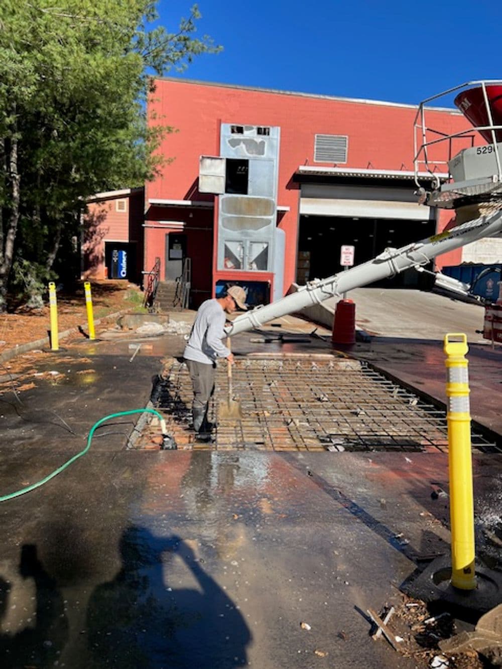 Worker preparing concrete at a construction site with a concrete pump and red building in background.