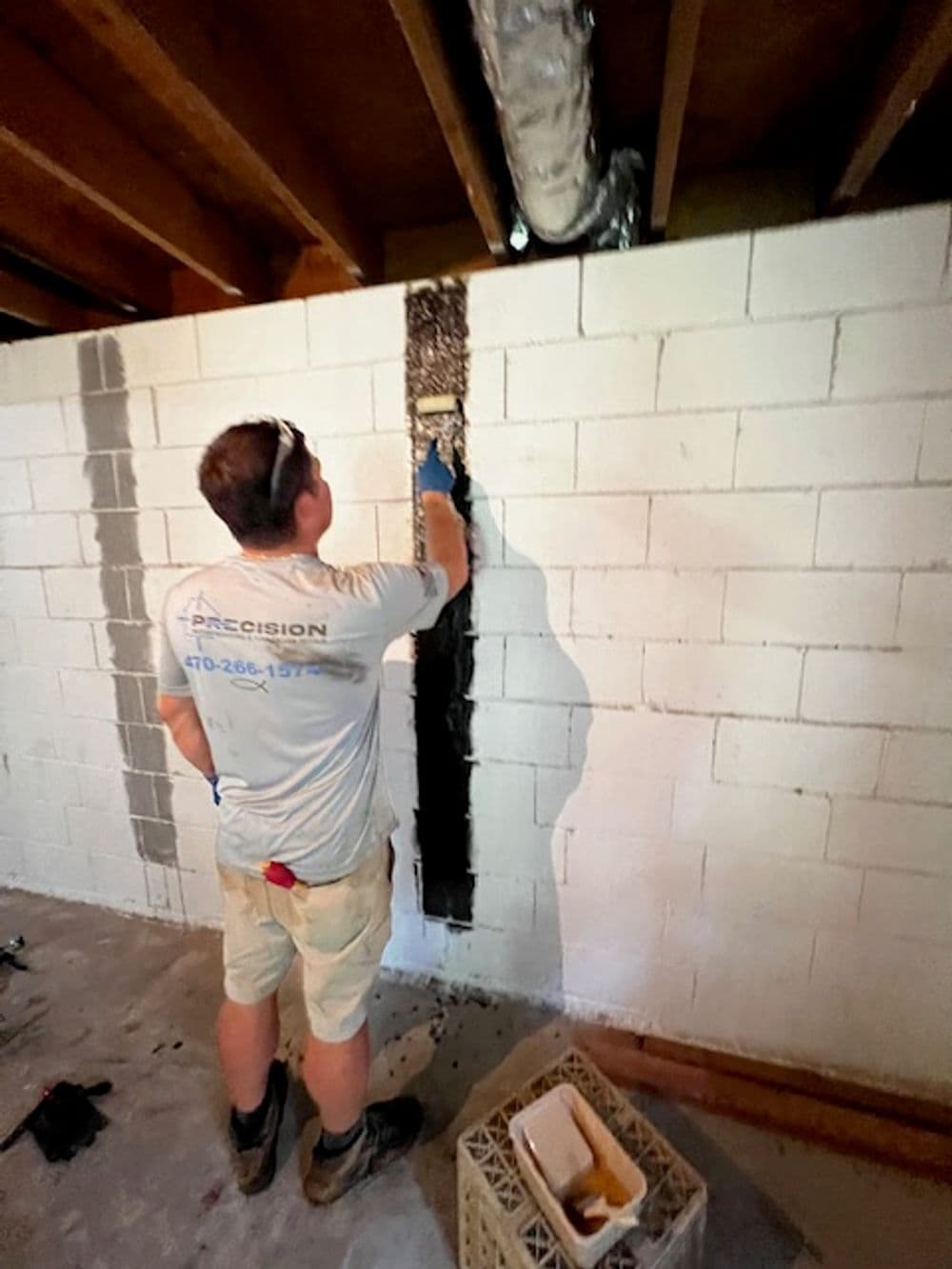 Construction worker repairing a basement wall with a trowel, surrounded by tools.
