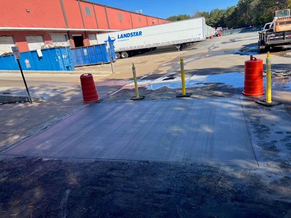 Concrete patch in a warehouse loading area with barriers and truck in the background.