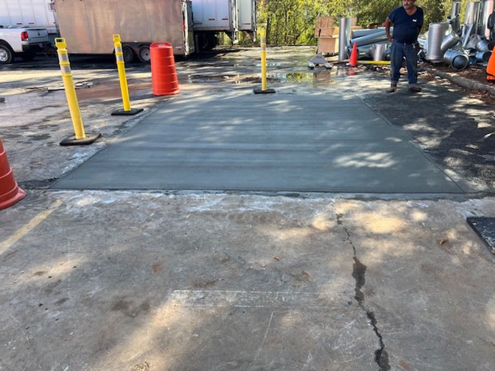 Worker smoothing freshly poured concrete in a construction area with traffic cones and barriers.