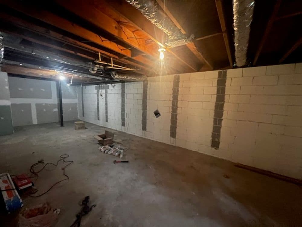 Empty basement with exposed beams, concrete walls, and overhead lighting.