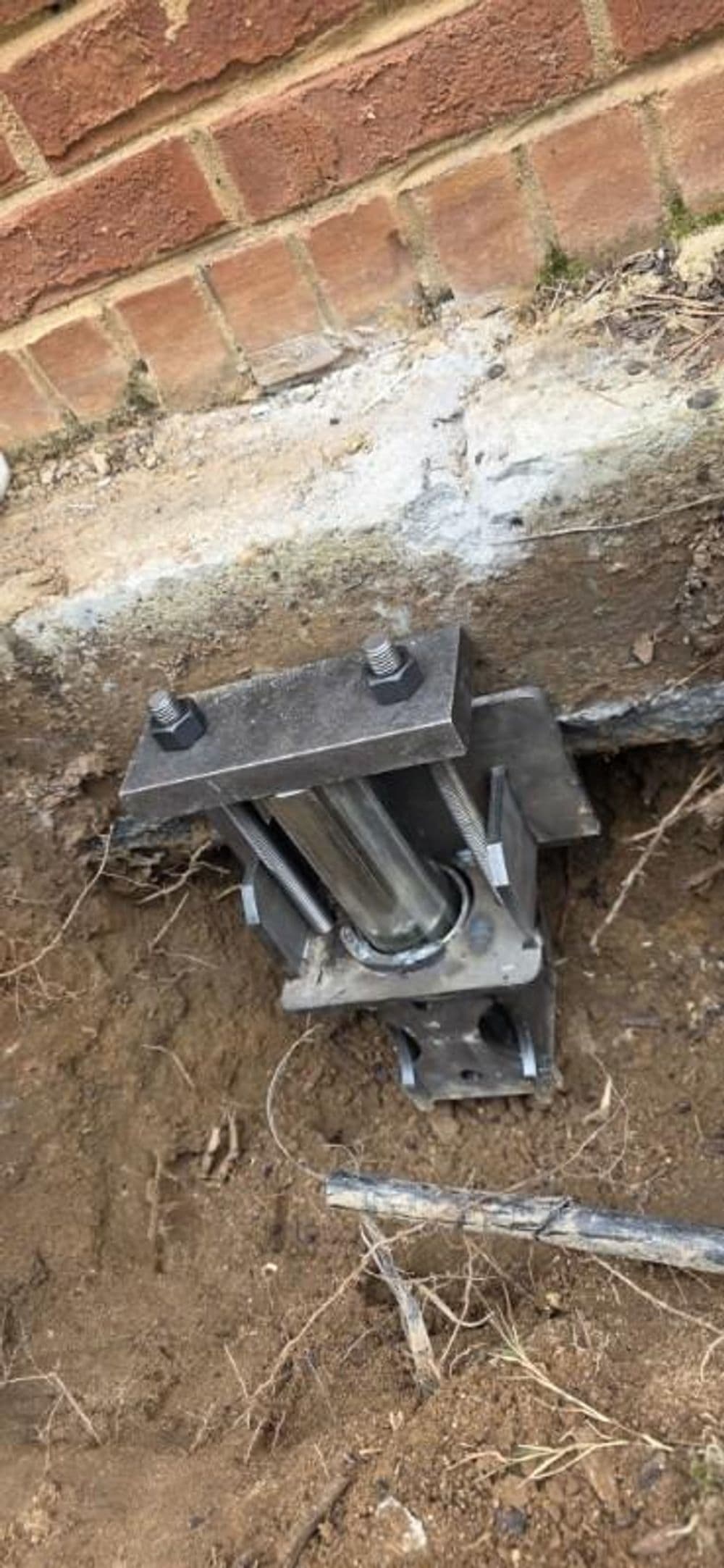 Hydraulic jack installed in ground near brick wall for foundation repair.