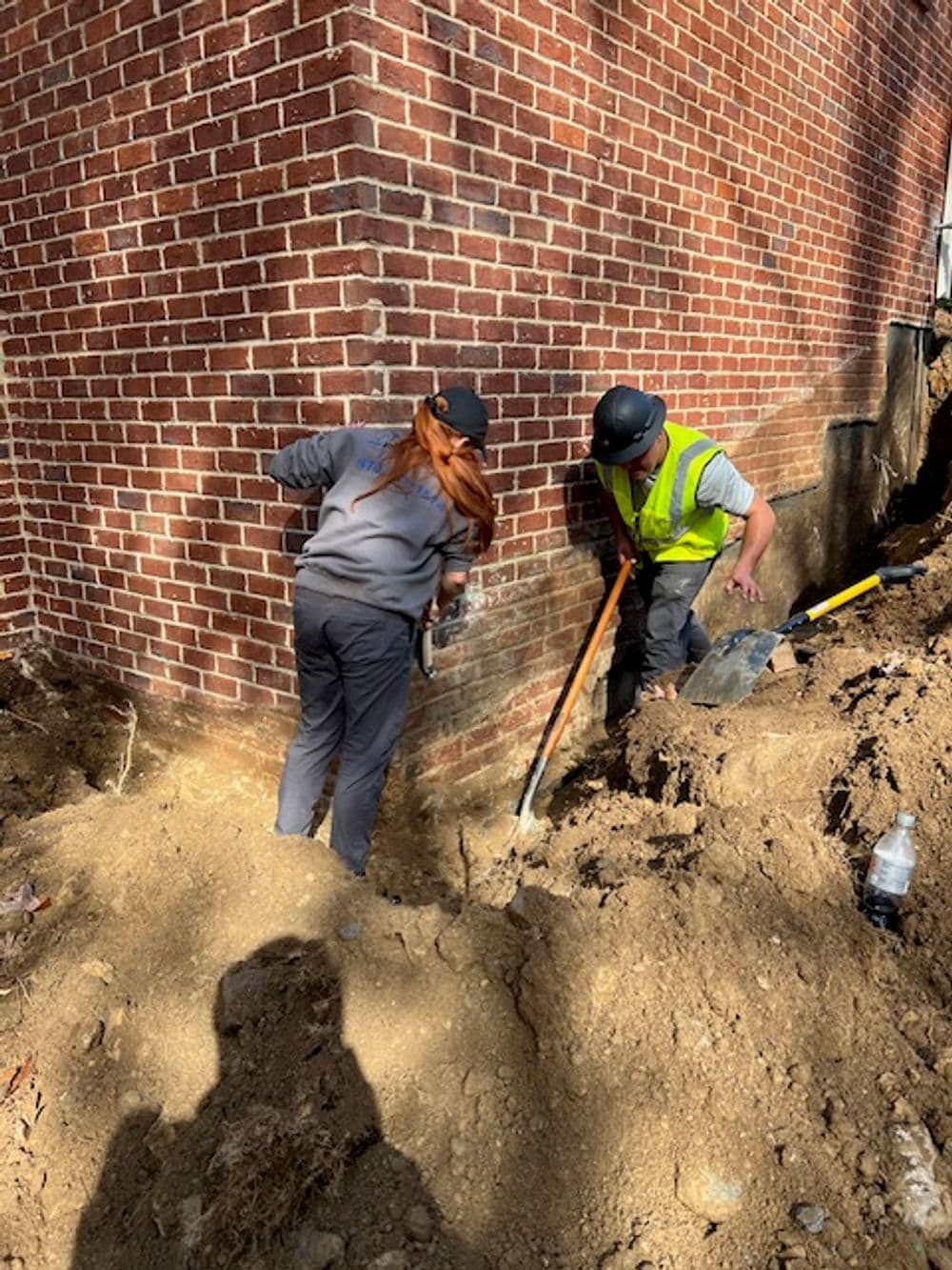 Workers excavating soil near a brick wall, focused on a construction project.