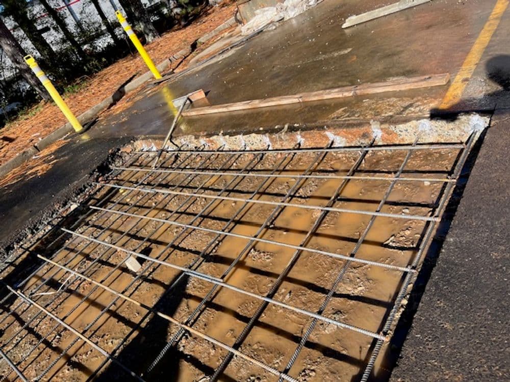 Construction site showing exposed rebar and water on a broken concrete slab. Safety barriers present.