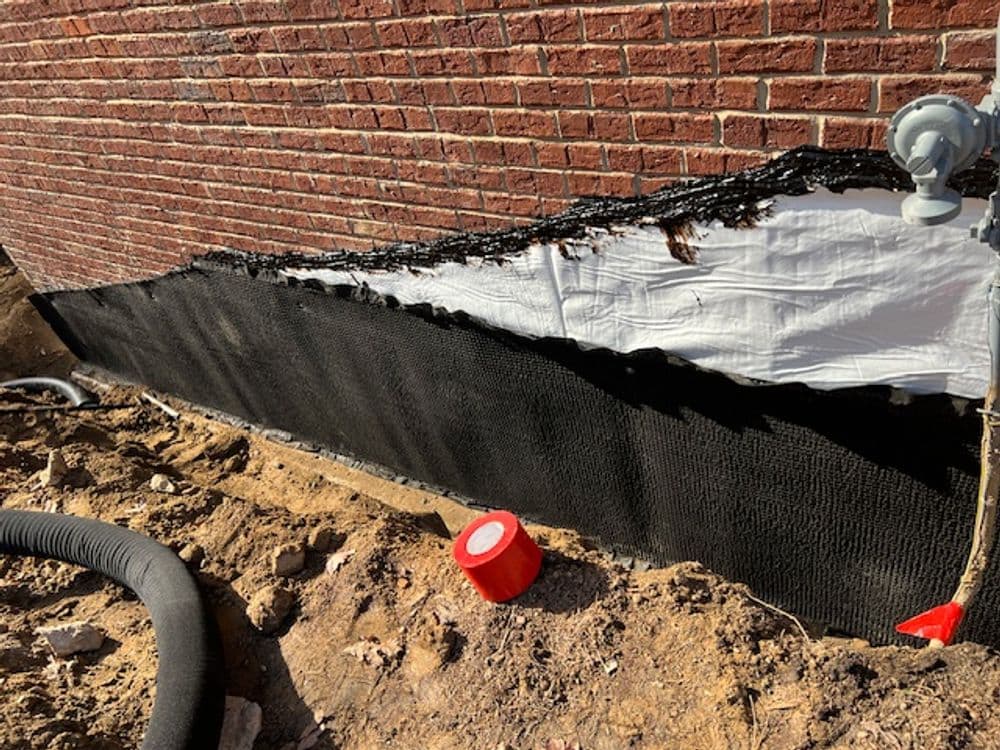 Exterior foundation waterproofing installation with exposed soil and drainage materials.