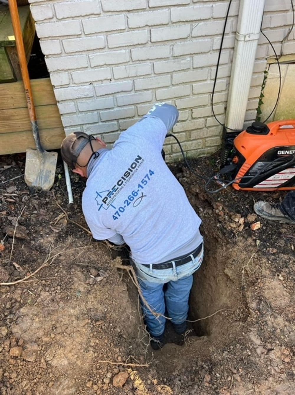 Worker digging a trench near a building for plumbing installation or repair.