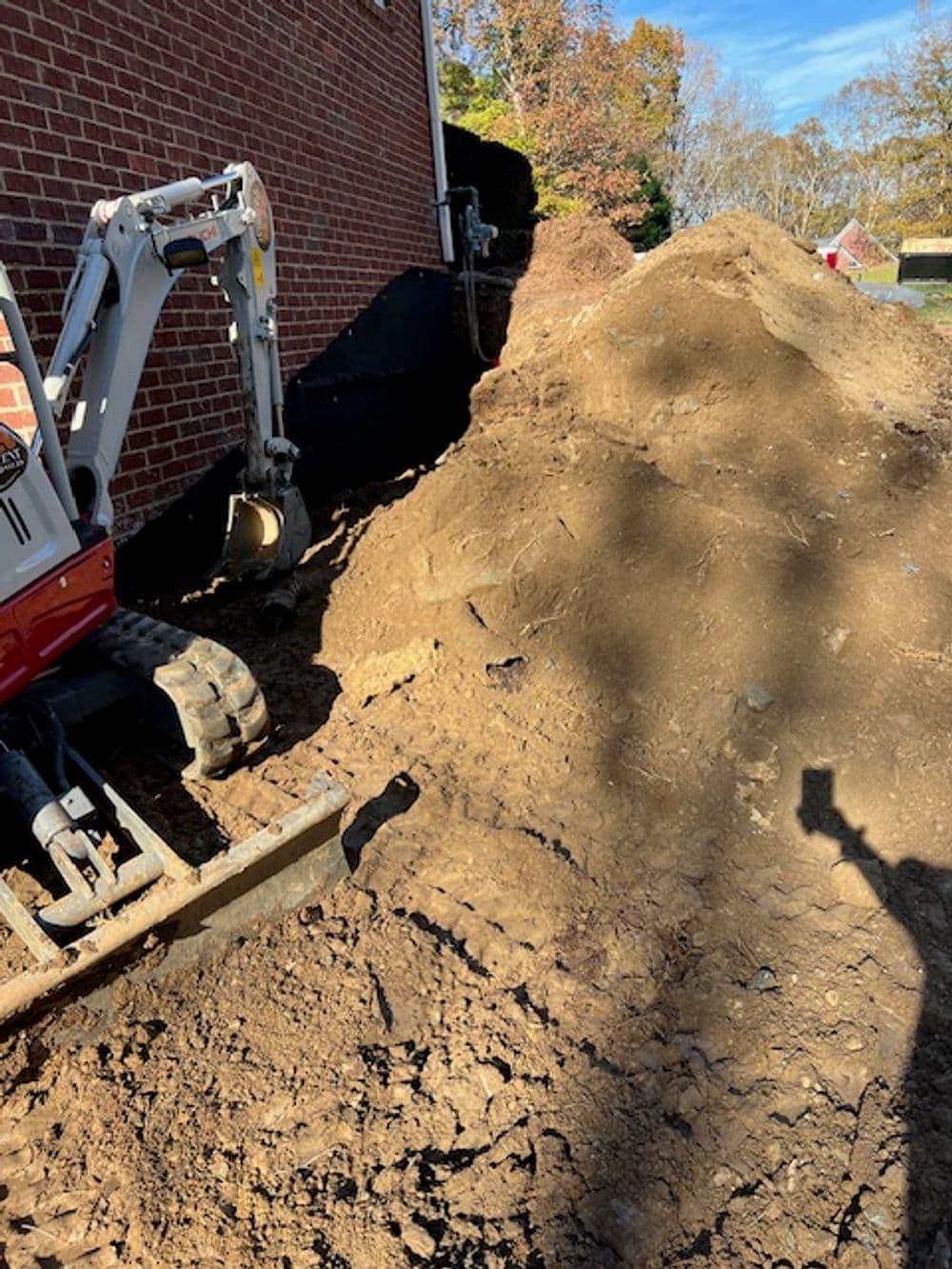 Excavator next to a large dirt pile beside a brick house in a construction site.