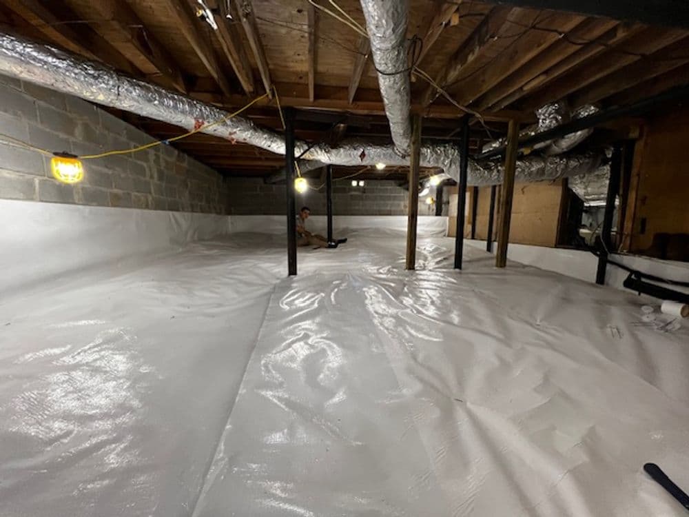 Crawl space with plastic sheeting, exposed beams, and lighting for moisture control.
