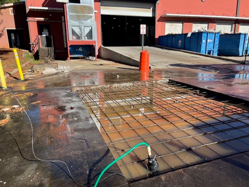 Construction site with exposed concrete rebar and water accumulation near a loading dock.