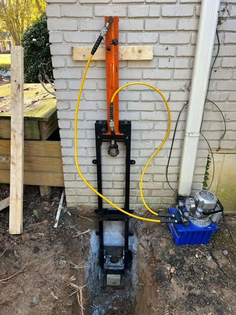 Hydraulic piering system installed against a brick wall for foundation stabilization.