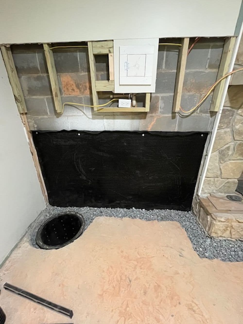 Basement wall renovation with drainage system, gravel, and exposed electrical panel.