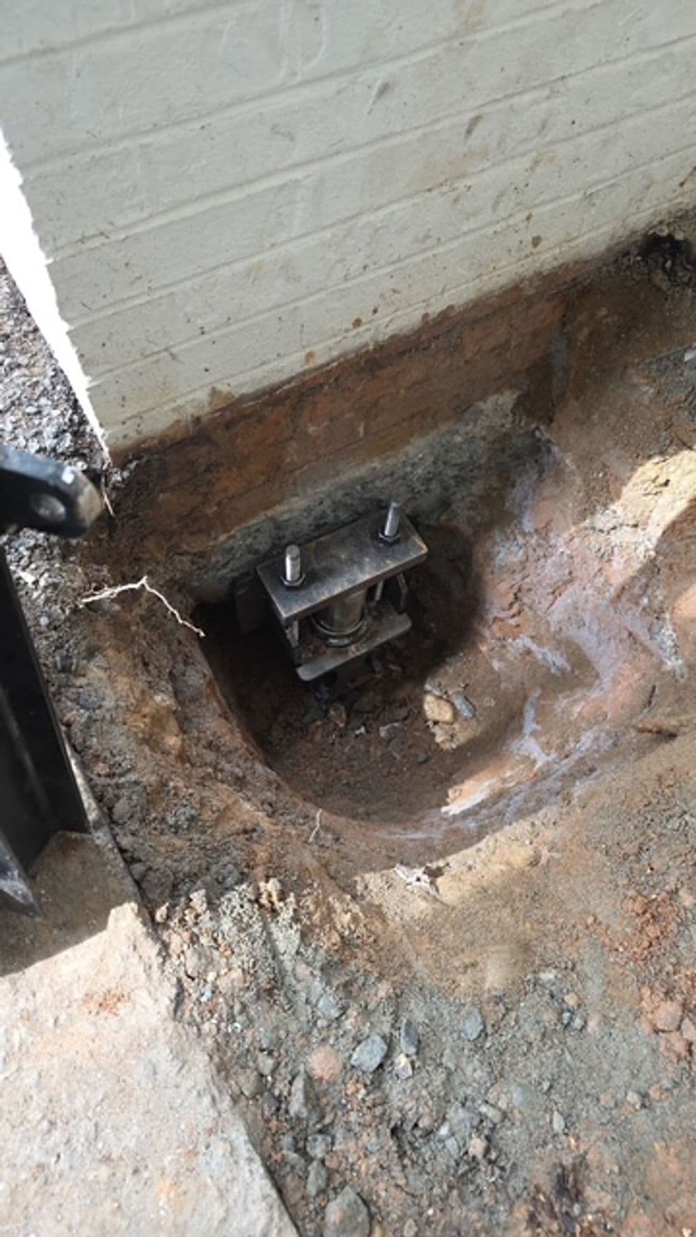 Concrete footing with metal bracket for structural support installation near a foundation.