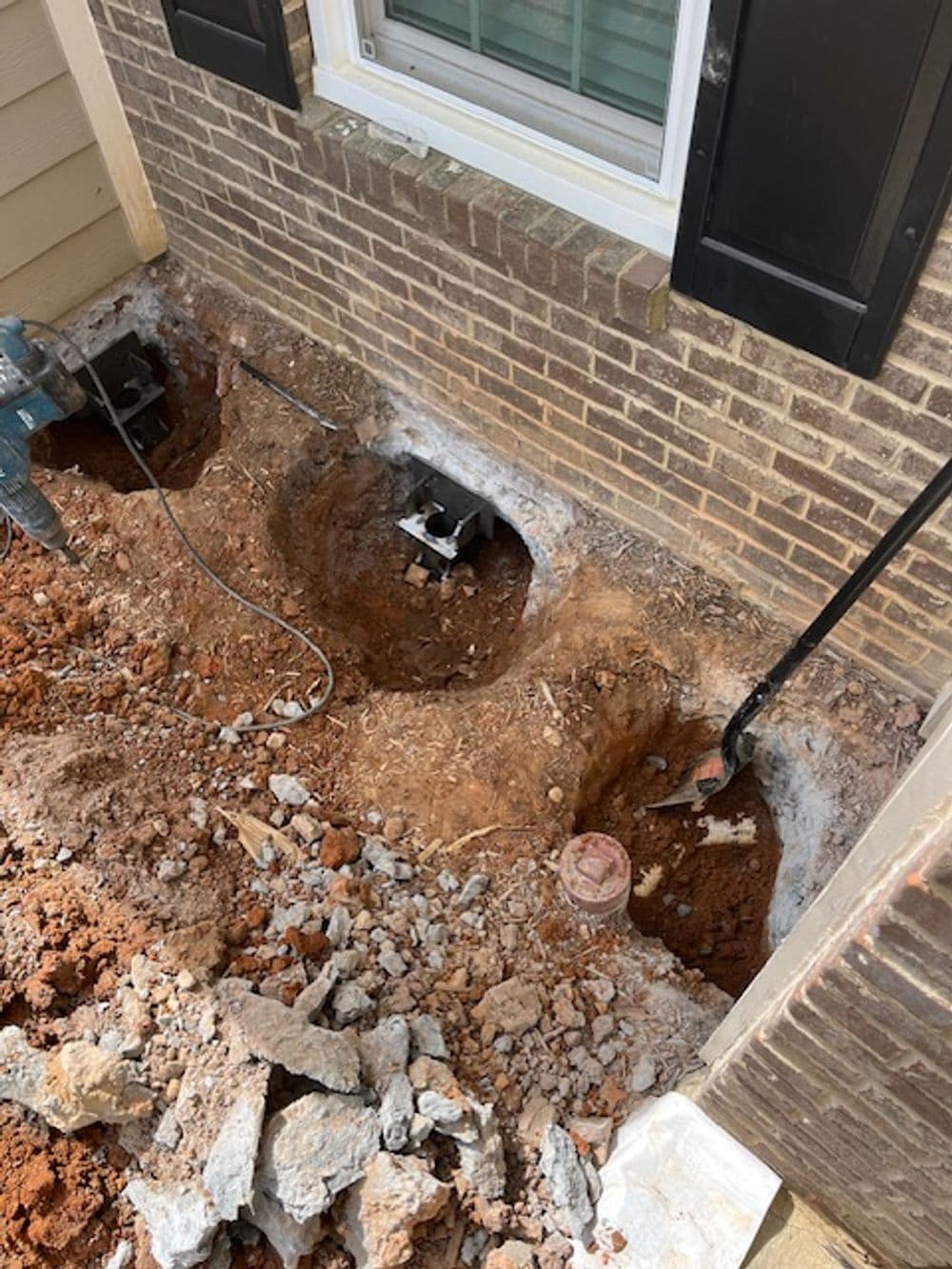 Excavated area beside a brick wall showing utility pipes and tools for home renovation.
