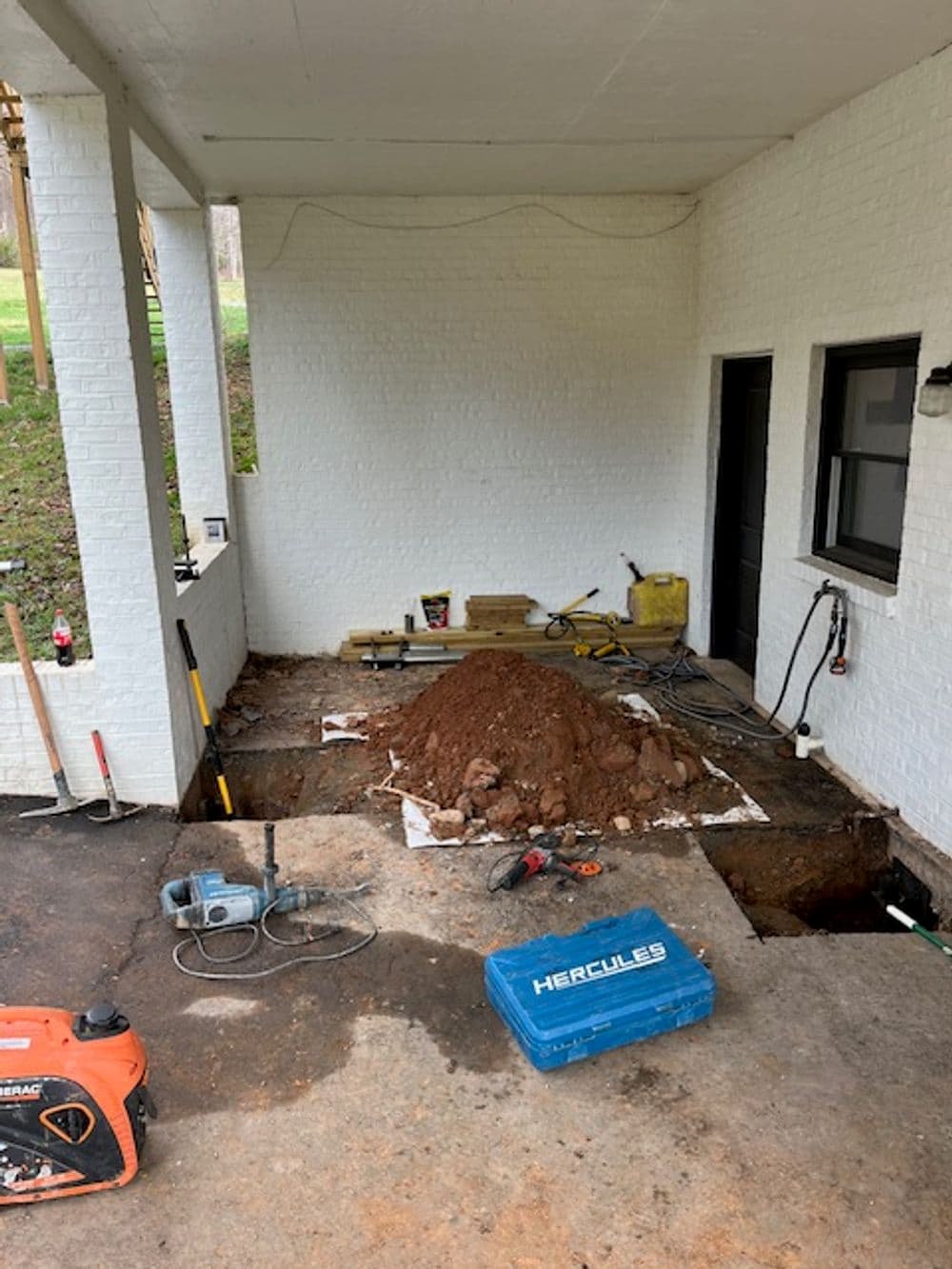 Pipes and equipment beside a building foundation on gravel surface.